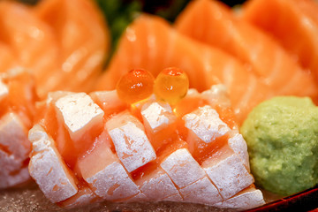 Closeup Salmon fish sliced Sashimi on ice in black red bowl with Salmon roe and Wasabi at the japanese restaurant, as seafood background. Japanese Foods Concept.