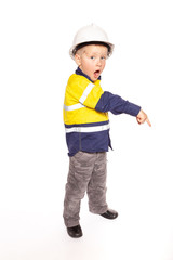 Young blond caucasian boy pointing down with a shocked look role playing a construction worker supervisor in a yellow and blue hi-viz shirt, boots, with white hard hat, minus hammer and tape measure