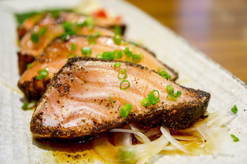 Premium quality  fish sliced, Salmon Steak with black pepper and sauce in white plate, on the wooden table background. at the japanese restaurant. Japanese Foods Concept.