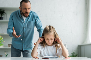 selective focus of kid covering ears near screaming father at home