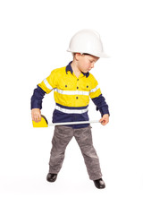 Young blond caucasian boy measuring something role playing as a construction worker in a yellow and blue hi-viz shirt, boots, white hard hat, and tape measure.