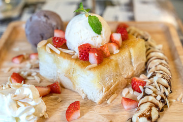 Strawberry honey toast with ice cream on wood plate dish.