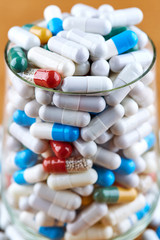 Many colorful pills in transparent glass on wooden background