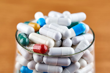 Many colorful pills in transparent glass on wooden background