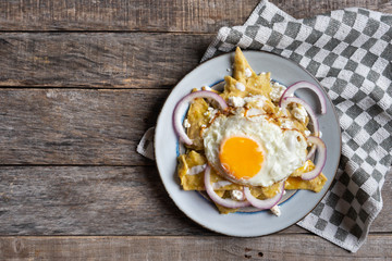 Mexican food: tasty green chilaquiles with fried egg, onion and fresh cheese