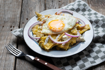 Mexican food: tasty green chilaquiles with fried egg, onion and fresh cheese