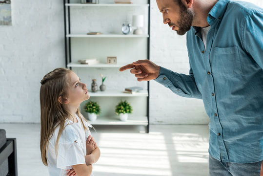 Upset Kid Standing With Crossed Arms And Looking At Angry Father