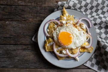 Mexican food: tasty green chilaquiles with fried egg, onion and fresh cheese