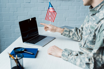 cropped view of military man pointing with finger at laptop with blank screen