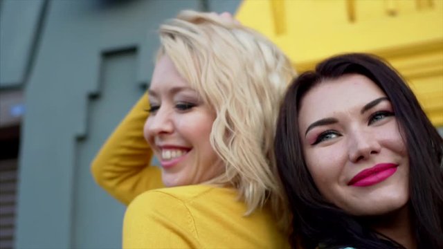 Slow motion. Portrait of brunette and blonde women posing back to back at photo shoot
