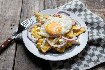 Mexican food: tasty green chilaquiles with fried egg, onion and fresh cheese