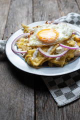 Mexican food: tasty green chilaquiles with fried egg, onion and fresh cheese