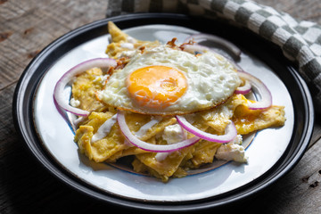 Mexican food: tasty green chilaquiles with fried egg, onion and fresh cheese