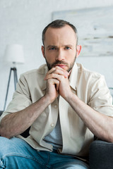 bearded and handsome man sitting on sofa at looking at camera