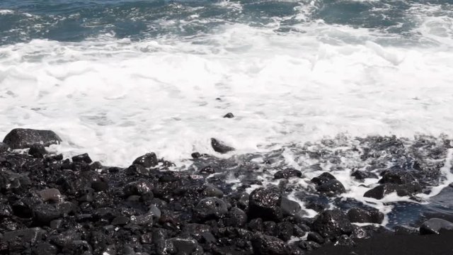 closeup slow motion capture of waves breaking on rocks on black sand beach in hawaii