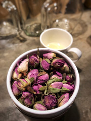 Pink Rose tea in package and white cup on the cement table with cafe light and glass bottle background.