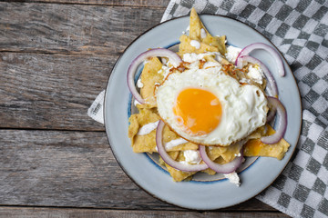 Mexican food: tasty green chilaquiles with fried egg, onion and fresh cheese