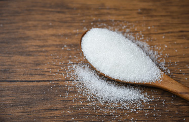 Fototapeta na wymiar White sugar on wooden spoon on wood background