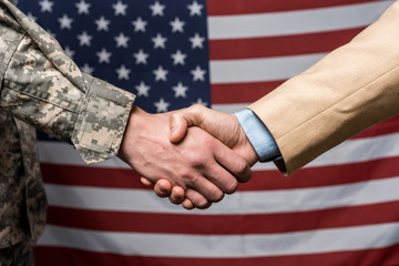 Selective focus military men shaking hands near American flag