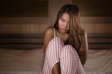 Fototapeta na wymiar dramatic lifestyle portrait of young sad and depressed Asian Indonesian woman in pajamas sitting desperate on bed suffering pain and depression feeling lonely