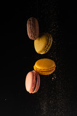 Colored macaroons, French cookies, colored levitates with cocoa powder on a black background