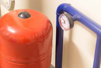 The steel pipe of blue color with a manometer stands next to the water tank of orange color