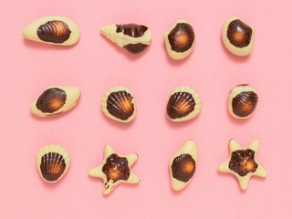 Candies made of white and dark chocolate stacked on a pink background. Flat lay.