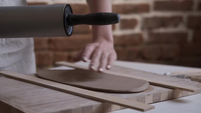 Interesting hobby. Jewelry designer pressing and flattening the clay with rolling pin. Woman hands making clay product. Work closeup. Process of creating jewelry in creative studio. Education online