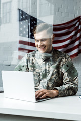 happy young soldier in camouflage uniform using laptop in office