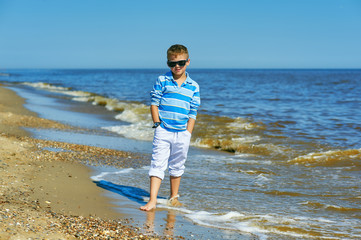 Beautiful boy posing on the seaside on a summer day . The child wears light jeans and a t-shirt
