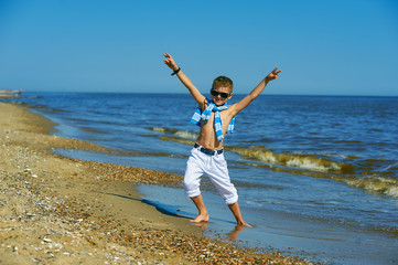 Beautiful boy posing on the seaside on a summer day . The child wears light jeans and a t-shirt