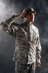 soldier in military uniform and cap giving salute on black with smoke