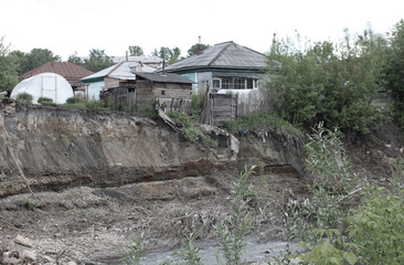 Fototapeta na wymiar old ruined wooden house on the edge of a cliff dangerously crumbling land on the river Bank in a Siberian village