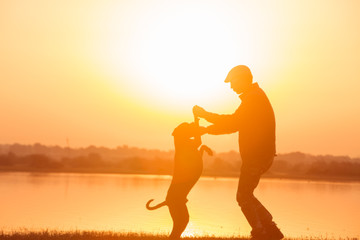 Fototapeta na wymiar Man playing with his dog near the lake at sunrise unfocused background