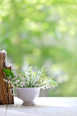 Lily of the valley in cup and book on white table. symbol of spring season. concept spring holiday, hello may, romantic spring time, inspiring mood. beautiful spring composition. copy space