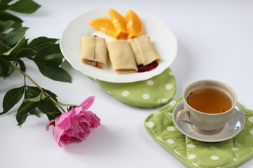 breakfast consisting of pancakes with berries and orange slices and a cup of tea