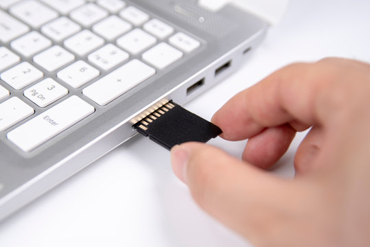 Human hand plugging in an SD media card into the personal laptop computer on white background.