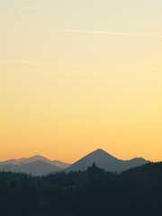 Morning landscape with mountains and orange sky at sunrise with sun reflecting. Evening sunset on the horizon of hills with snow and sun rays.