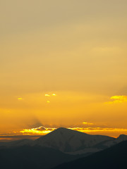 Morning landscape with mountains and orange sky at sunrise with sun reflecting. Evening sunset on the horizon of hills with snow and sun rays.