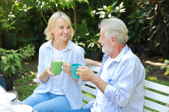 caucasian elderly couple with blue shirt and blue jean sitting and drinking coffee in garden during summer time on wedding anniversary day - Powered by Adobe