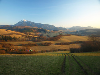 Morning landscape with mountains and blue sky at sunrise with sun reflecting. Evening sunset on the horizon of hills with white snow and green meadow