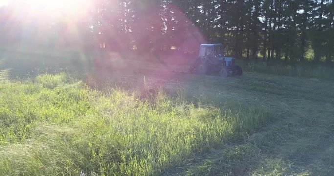 upper view blue tractor with mower drives along farmland and mows grass under scorching sun