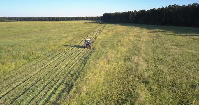 upper view mowing machine drives cutting off grass with blade on farmland surrounded by high trees