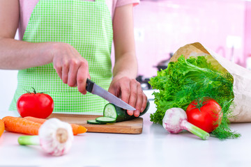 Woman in apron chopping fresh organic cucumber on cutting board for cooking vegetable dishes and salads at kitchen. Healthy clean food and balanced diet