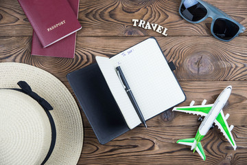 Flat lay traveler accessories on wooden background with straw hat, passport, airplane, and sunglasses.  Top view travel and planning summer vacation concept. 