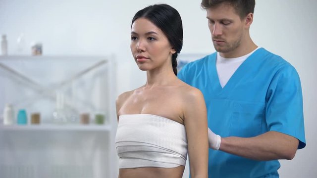 Male plastic surgeon applying elasto-fit breast female patient, compression