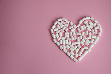 heart laid out of white and pink mini marshmallows on a pink background
