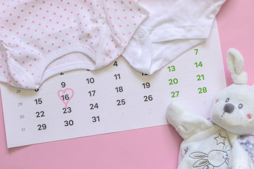 Set of newborn accessories in anticipation of  child - calendar with circled number 16 (sixteen), baby clothes, toys on pink background. Copy space, flat lay, top view.