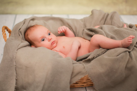 Newborn naked baby is lying in wicker basket. Basket on white wooden background. Newborn photo shoot