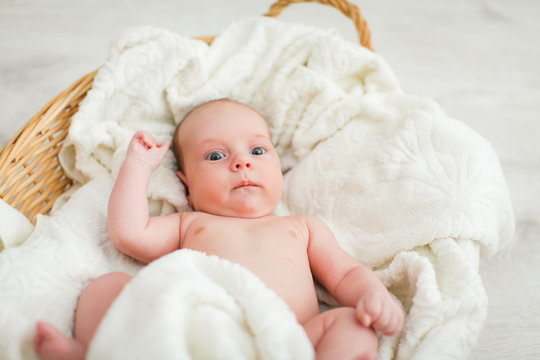Newborn naked baby is lying in wicker basket. Basket on white wooden background. Newborn photo shoot.